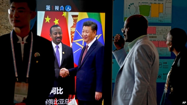 在北京举行中非合作论谈期间，非洲代表团成员走过正在播放中国国家主席习近平与埃塞俄比亚总理艾哈迈德握手的视频画面。（2018年9月3日）