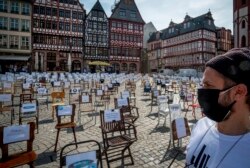 A man with a face mask watches empty chairs with names of bars and restaurants on the Roemerberg square in Frankfurt, Germany, April 24, 2020. Due to the coronavirus all bars and restaurants in Germany are still closed.