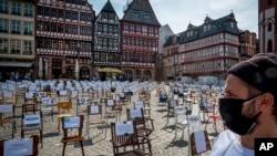 A man with a face mask watches empty chairs with names of bars and restaurants on the Roemerberg square in Frankfurt, Germany, April 24, 2020. Because of the coronavirus, all bars and restaurants in Germany are still closed. 