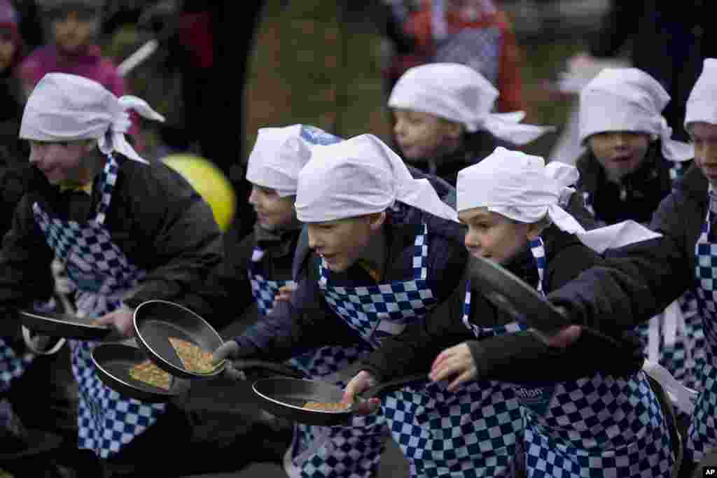 Ni&ntilde;os de una escuela local corren durante una competencia anual de panqueques como parte de las celebraciones por el carnaval en el pueblo de Olney, en Inglaterra.