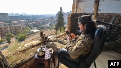 A fighter affiliated with Syria's new administration checks his phone as he sits outside the defunct Mezzeh military prison overlooking the capital, Damascus, Jan. 2, 2025.