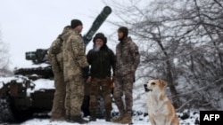 Esta fotografía tomada el 13 de diciembre de 2023 muestra a un perro sentado en la nieve junto a una tripulación de tanque ucraniano en una posición cerca de la ciudad de Bakhmut, región de Donetsk, en medio de la invasión rusa de Ucrania.