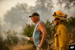 Jim Berglund sprays water while defending his home as a wildfire approaches, July 8, 2017, near Oroville, Calif. Although flames leveled Berglund's barn, his home remained unscathed as the fire passed.