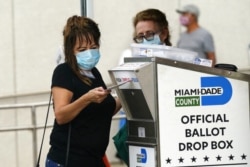 FILE - An election worker places a vote-by-mail ballot into an official ballot drop box outside a voting site in Miami, Fla.