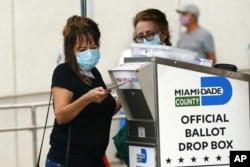 FILE - An election worker places a vote-by-mail ballot into an official ballot drop box outside a voting site in Miami, Fla.