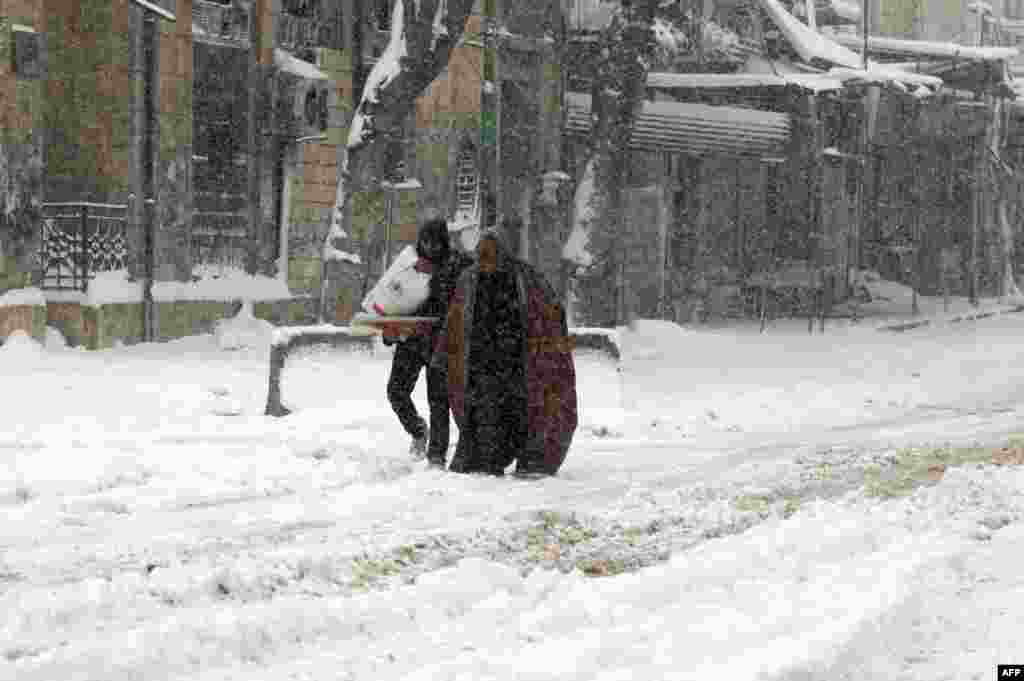 Dua pria Suriah berjalan di jalanan yang diselimuti salju di kota Maaret al-Numan, provinsi Idlib.