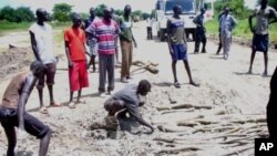 Trucks and passengers wait while local youths repair potholes on the Juba-Bor road in South Sudan