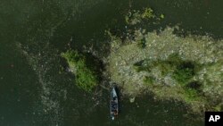 FILE - A boat moves through garbage floating on the basin of the Cerron Grande hydroelectric dam near Potonico, El Salvador, Sept. 25, 2022. 