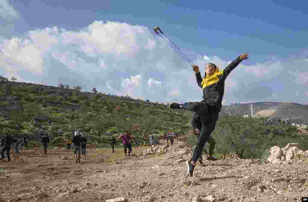 Palestinian protesters use slingshots against Israeli soldiers during clashes, at the outskirts of the West Bank village of Mughayer, north of Ramallah.