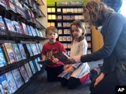 Elizabeth Gilless, of Memphis, Tenn., shows her children John, 3, and Ellen, 5, a movie from the children's section at the last Blockbuster on the planet in Bend, Ore., on Tuesday, March 12, 2019. (AP Photo/Gillian Flaccus)