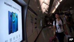 FILE - A woman walks past an advertisement for Huawei at a subway station in Hong Kong, Dec. 5, 2018. 