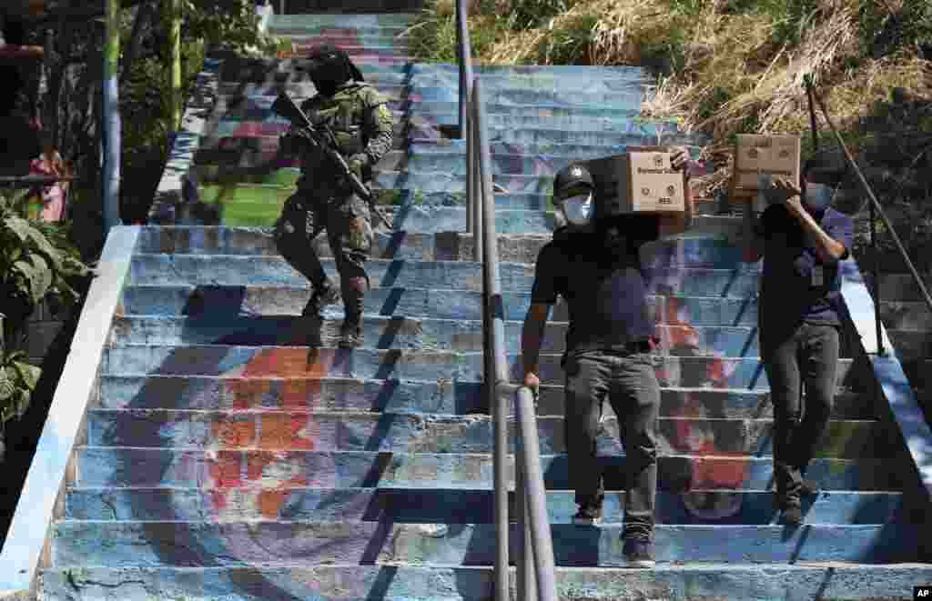 A soldier escorts volunteers delivering boxes of donated food to people affected by the COVID-19 pandemic, in San Salvador, El Salvador, March 13, 2021.