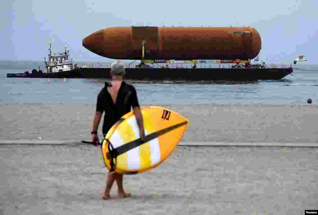 A paddle boarder makes his way to the water as the space shuttle fuel tank ET-94 arrives by barge for its eventual placement at the California Science Center in Marina del Rey, California, USA.
