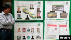 FILE - A journalist looks at posters detailing the arrest operation of a suspect in the death of U.S. Drug Enforcement Administration Special Agent James "Terry" Watson, in Bogota.