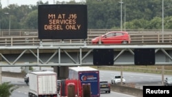 Trucks drive past a fuel warning sign on the M1 motorway amid a fuel shortage, in Luton, England, Sept. 30, 2021.
