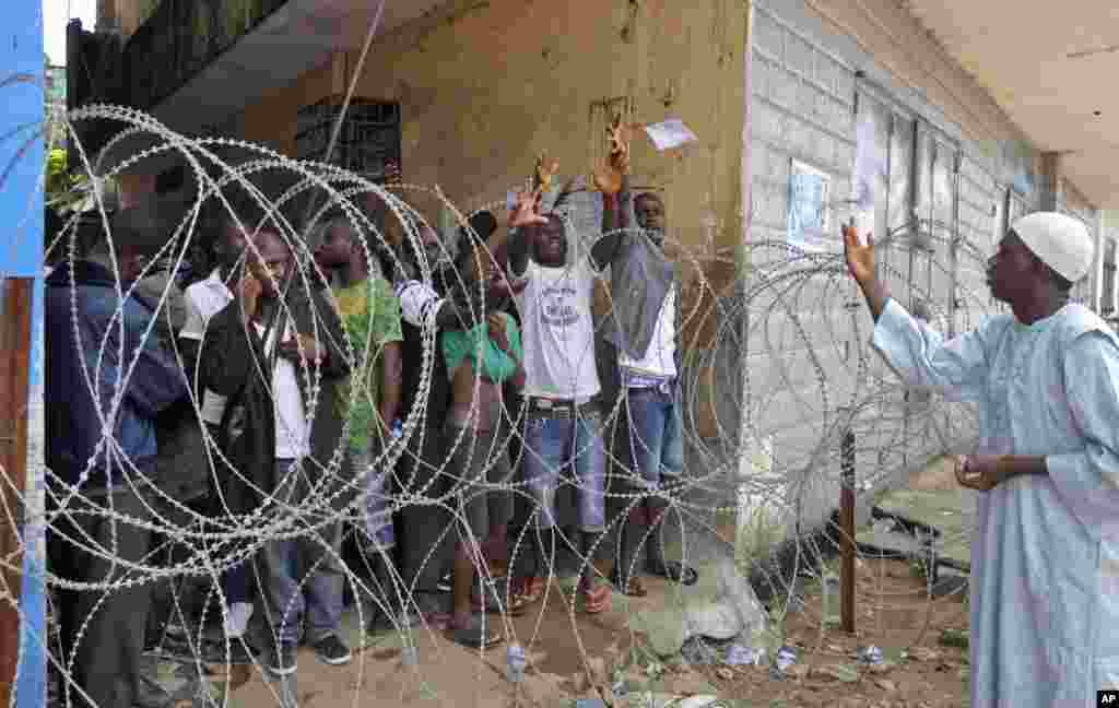 A man working for a humanitarian group throws small bags of water to the residents behind the fence as they wait for a second consignment of food from the Liberian Government, at the West Point area, Monrovia, Liberia, Aug. 22, 2014.