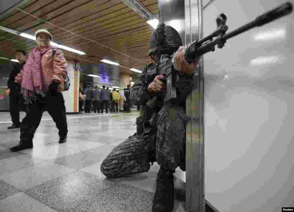 Seorang tentara Korea Selatan siaga di sebuah stasiun kereta bawah tanah, sementara seorang wanita melihat aksi tersebut, selama latihan anti-teror di Seoul. 