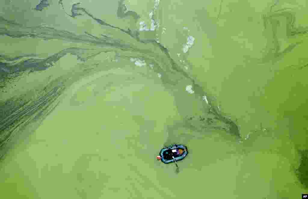 A fisherman in a rubber boat is surrounded by rotting cyanobacteria in the Kyiv Water Reservoir near Kyiv, Ukraine.