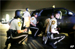 FILE - Police take cover behind a vehicle during a protest in Ferguson, Missouri, Aug. 9, 2015. Some authorities blame a recent spike in homicides in select U.S. cities on the "Ferguson effect." Others disagree.