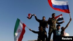 Syrians wave Iranian, Russian and Syrian flags during a protest against U.S.-led air strikes in Damascus, Syria, April 14, 2018.