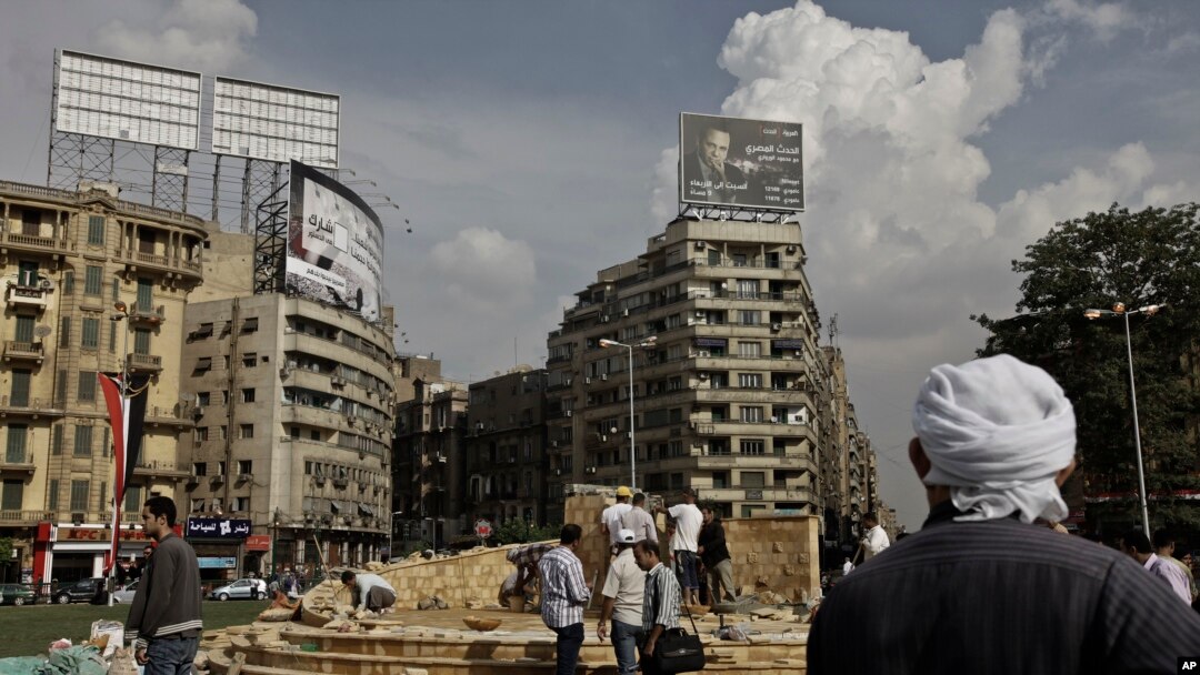 In this Sunday, Nov. 17, 2013 photo, an Egyptian man looks at municipality laborers working on a memorial base two days before the commemoration of deadly clashes with security forces in 2011, in Tahrir Square, Cairo. 