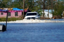 A truck drives through a flooded street in Lake Charles, La., Oct. 10, 2020, past a home with damage from Hurricane Laura, after Hurricane Delta moved through on Friday.