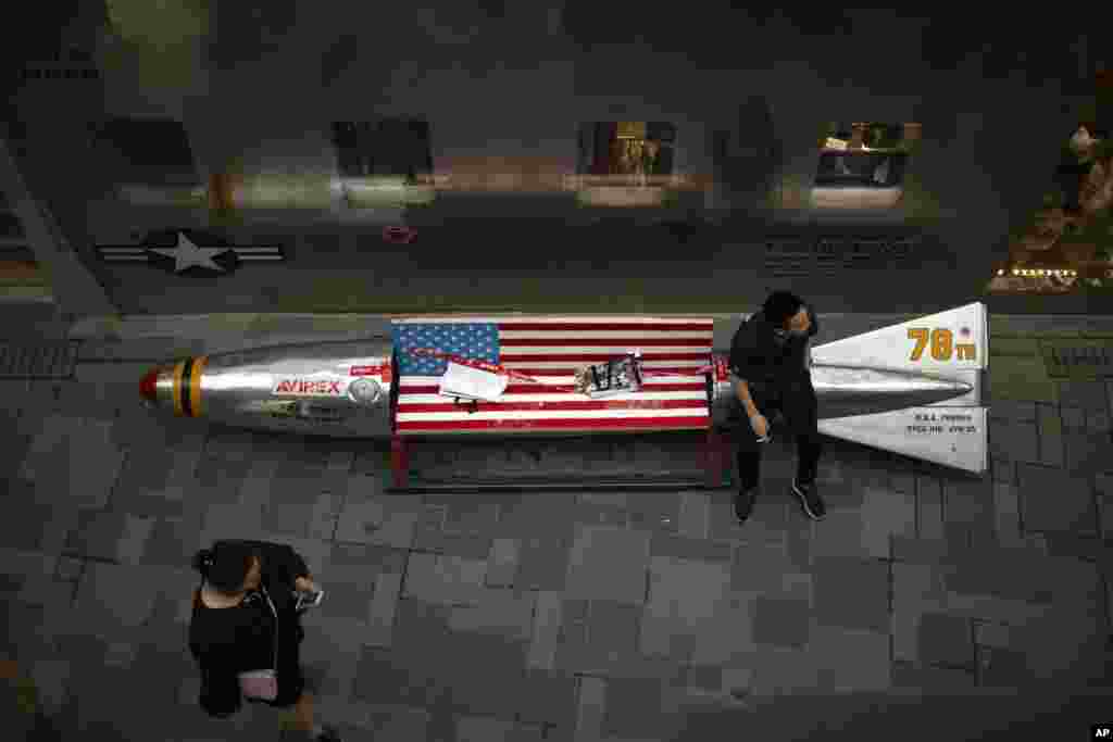 A man sits on a promotional gimmick in the form of a bomb and the U.S. flag outside a U.S. apparel shop at a shopping mall in Beijing, China. China said it&rsquo;s girded for a trade war with the U.S. and can give as good as it gets, but behind the official bravado lies a deep unease over trade friction with Washington.