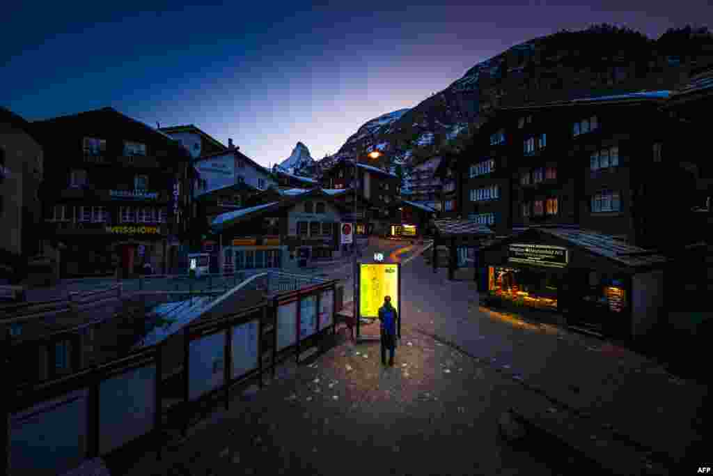 A person looks at an lit-up map board in the empty streets of the Alpine town of Zermatt, Switzerland, during the spread of COVID-19.
