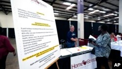 A list of benefits flanks Jon Stembridge, center, a human resource and safety manager with HomeStretch, a domestic manufacturer of upholstered reclining furniture, as he welcomes a potential applicant to his company's recruiting booth, Miss., Oct. 12, 2021. 