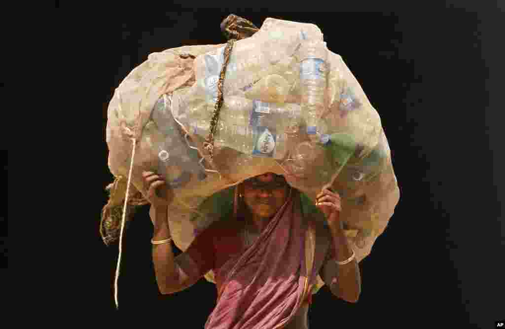 یک زن هندی کیسه بطری های پلاستیکی را برای بازیافت حمل می کند.