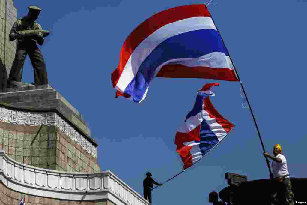 Para pengunjuk rasa anti-pemerintah melambaikan bendera nasional Thailand saat berkumpul dengan yang lainnya di Monumen Kemenangan di pusat kota Bangkok (13/1).