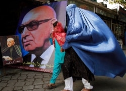 FILE - An Afghan woman with her daughter walks past a huge poster of Afghanistan's first president, Sardar Muhammad Daud Khan, and a small poster of current President Hamid Karzai in Jalalabad, Nangarhar province, Afghanistan, March 16, 2010.