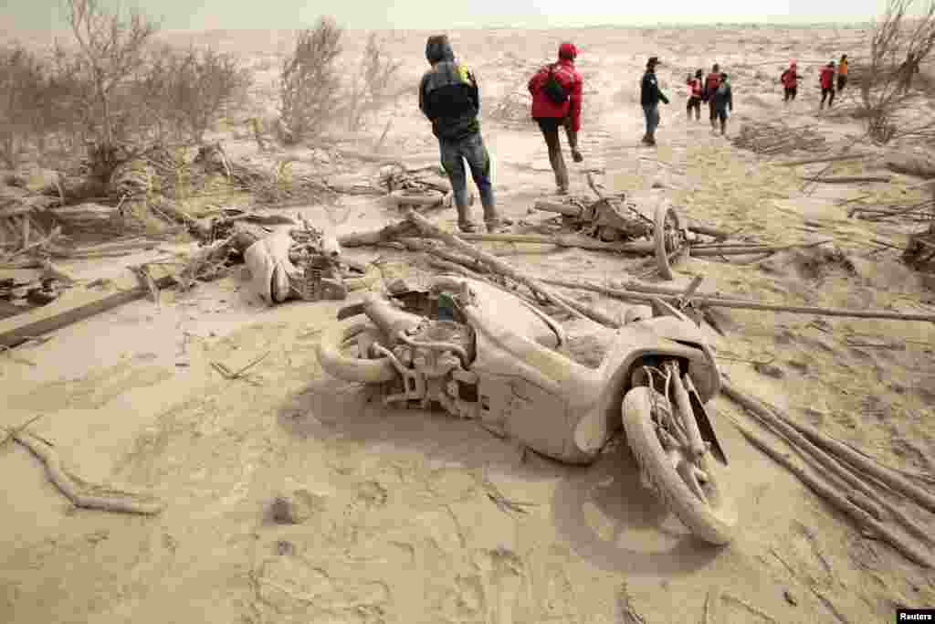 Ash-covered motorcycles are pictured as a rescue team walks by following the Mount Sinabung eruption at Suka Meriah village in Karo, North Sumatra province, Feb. 2, 2014.