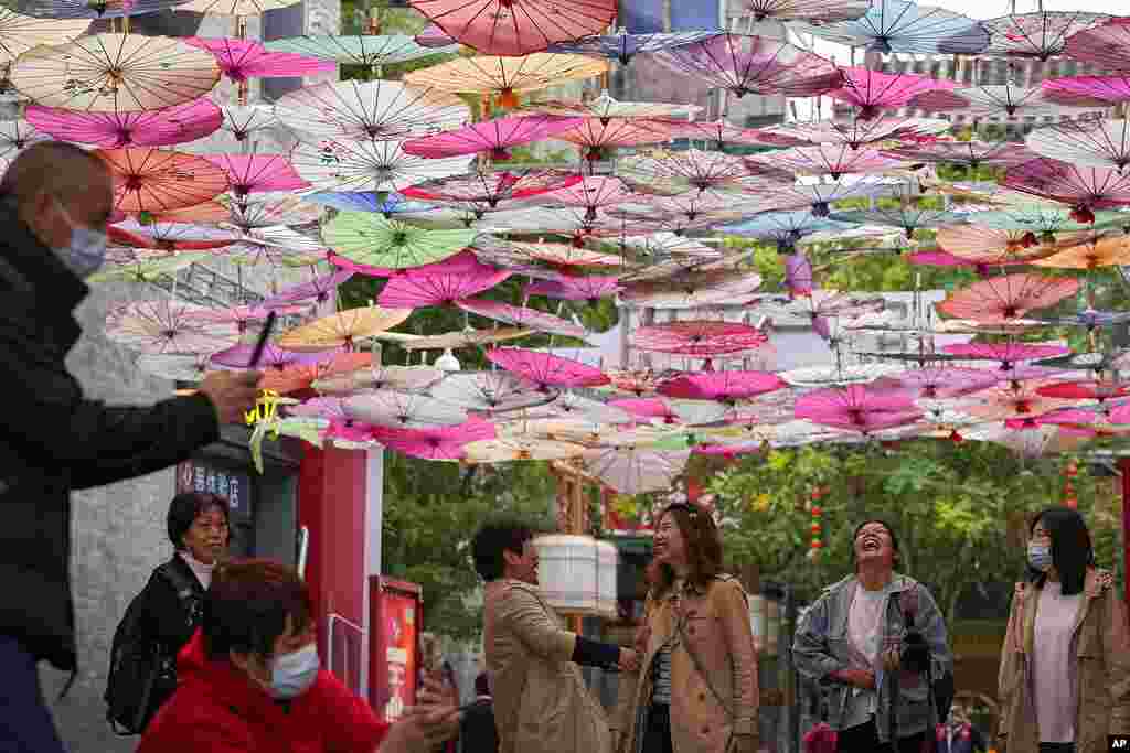 Women share a light moment as visitors wearing face masks take pictures underneath colorful umbrellas on display along a hutong alley near Qianmen Avenue, a popular tourist spot in Beijing.