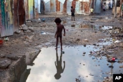 FILE - A child plays in a puddle in the seaside slum of Port-au-Prince, Haiti, Sept. 6, 2017.