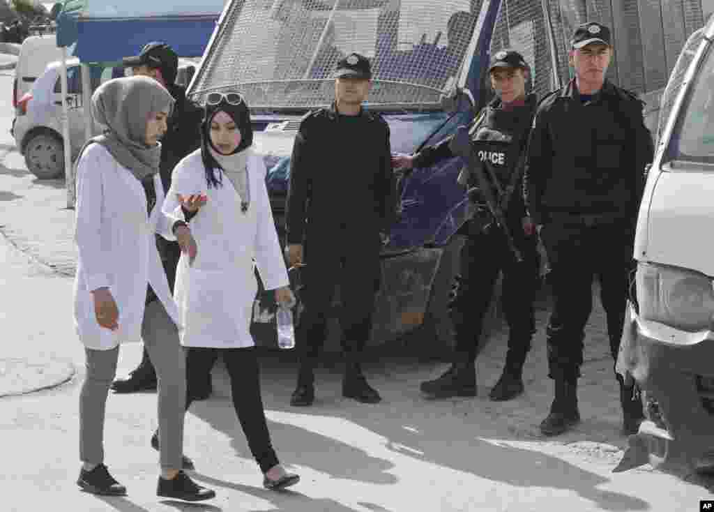 Tunisian police officers stand guard at the Charles Nicolle hospital while personnel pass by, in Tunis Tunisia, March 19, 2015.