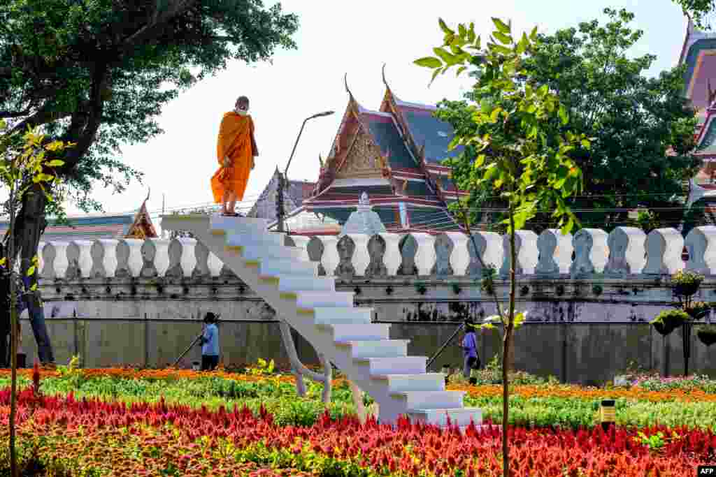 A Buddhist monk looks on from a staircase in the middle of a park in central Bangkok, Thailand.