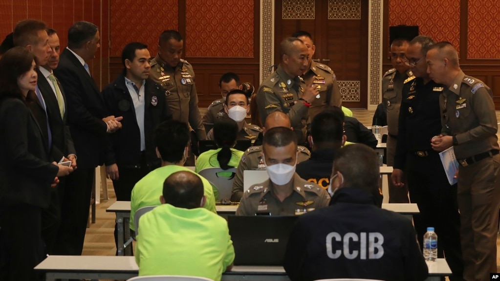 In this photo released by Thailand's Cyber Crime Investigation Bureau, policemen talk to suspects, wearing light green shirts, at the Cyber Crime Investigation Bureau in Bangkok, Thailand, March 22, 2023. 