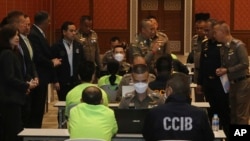 In this photo released by Thailand's Cyber Crime Investigation Bureau, policemen talk to suspects, wearing light green shirts, at the Cyber Crime Investigation Bureau in Bangkok, Thailand, March 22, 2023. 