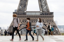 People wearing protective masks walk near the Eiffel Tower as the French tourism landmark reopened to visitors after being evacuated in Paris, France, Sept. 23, 2020.