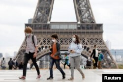 People wearing protective masks walk near the Eiffel Tower as the French tourism landmark reopened to visitors after being evacuated in Paris, France, Sept. 23, 2020.