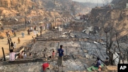 Rohingya refugees look at the remains of Monday's fire at the Rohingya refugee camp in Balukhali, southern Bangladesh, Tuesday, March 23, 2021. (AP Photo/ Shafiqur Rahman)