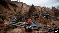 FILE - Manuel Espinosa holds his 4-month-old son as he takes a break from mining gold in La Pampa, located in the Madre de Dios region of Peru, May 2, 2014. 