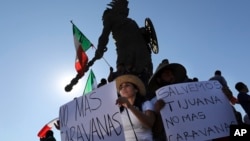 Para demonstran mengacungkan poster-porster bertuliskan, dalam bahasa Spanyol,protes-protes atas kedatangan ribuan kafilah migran Amerika Tengah, dalam unjuk rasa di sekitar patung penguasa Aztec Cuauhtemoc, di Tijuana, Meksiko, 18 November 2018. 