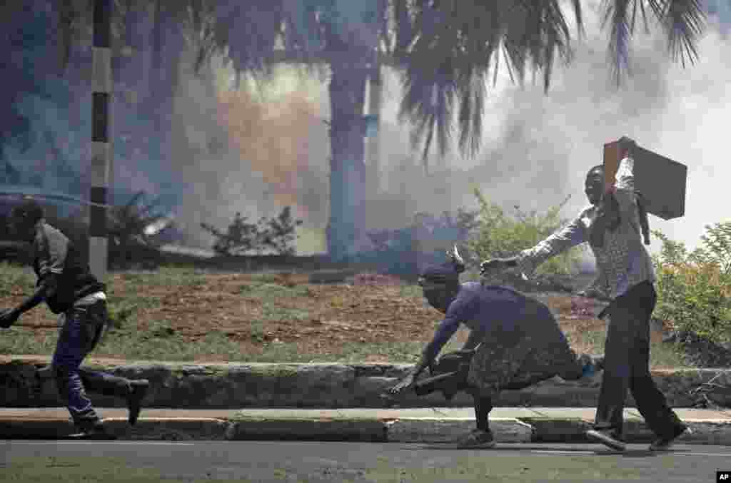 A passerby stumbles to the ground as she and opposition supporters, protesting over the upcoming elections, run for safety amid a cloud of tear gas fired by riot police in downtown Nairobi, Kenya.