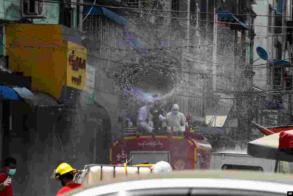 Members of Fire Service Department wearing full protective gear spray disinfectant from fire engine to curb the spread of the coronavirus on a street in Yangon, Myanmar.