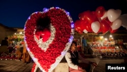 A man sits on a roadside next to a paper-flower decoration as he holds heart-shaped balloons, waiting for costumers on the ahead of Valentine's Day in Islamabad February 13, 2014. REUTERS/Mian Khursheed (PAKISTAN - Tags: SOCIETY) - RTX18R58