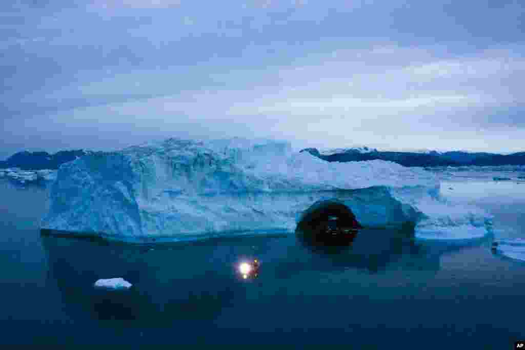 A boat navigates at night next to a large iceberg in eastern Greenland, Aug. 15, 2019. 