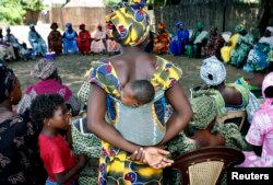 FILE - A mother carrying an infant on her back attends a meeting of women from several communities eradicating female genital mutilation, in Diabougo, Senegal.