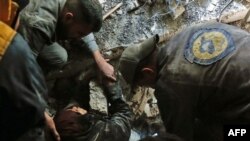 In this file photo, volunteers of the Syrian Civil Defense, known as the White Helmets, rescue a woman from the wreckage of a building after an airstrike in Douma, eastern Ghouta, March 19, 2018.